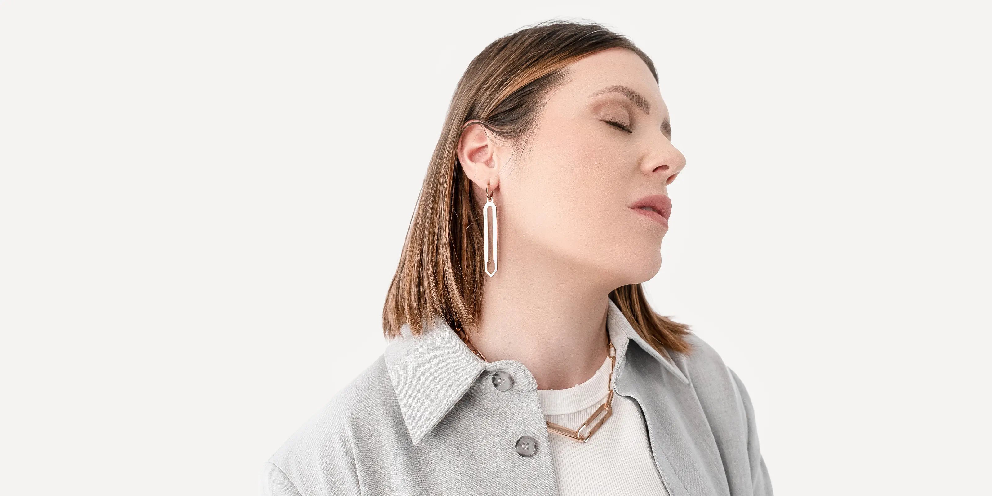 Weibliches Model trägt Forma Lamina Ohrringe und Forma Nexus Halskette, beide in Roségold aus hochwertigem 316L-Edelstahl, vor neutralem Hintergrund.