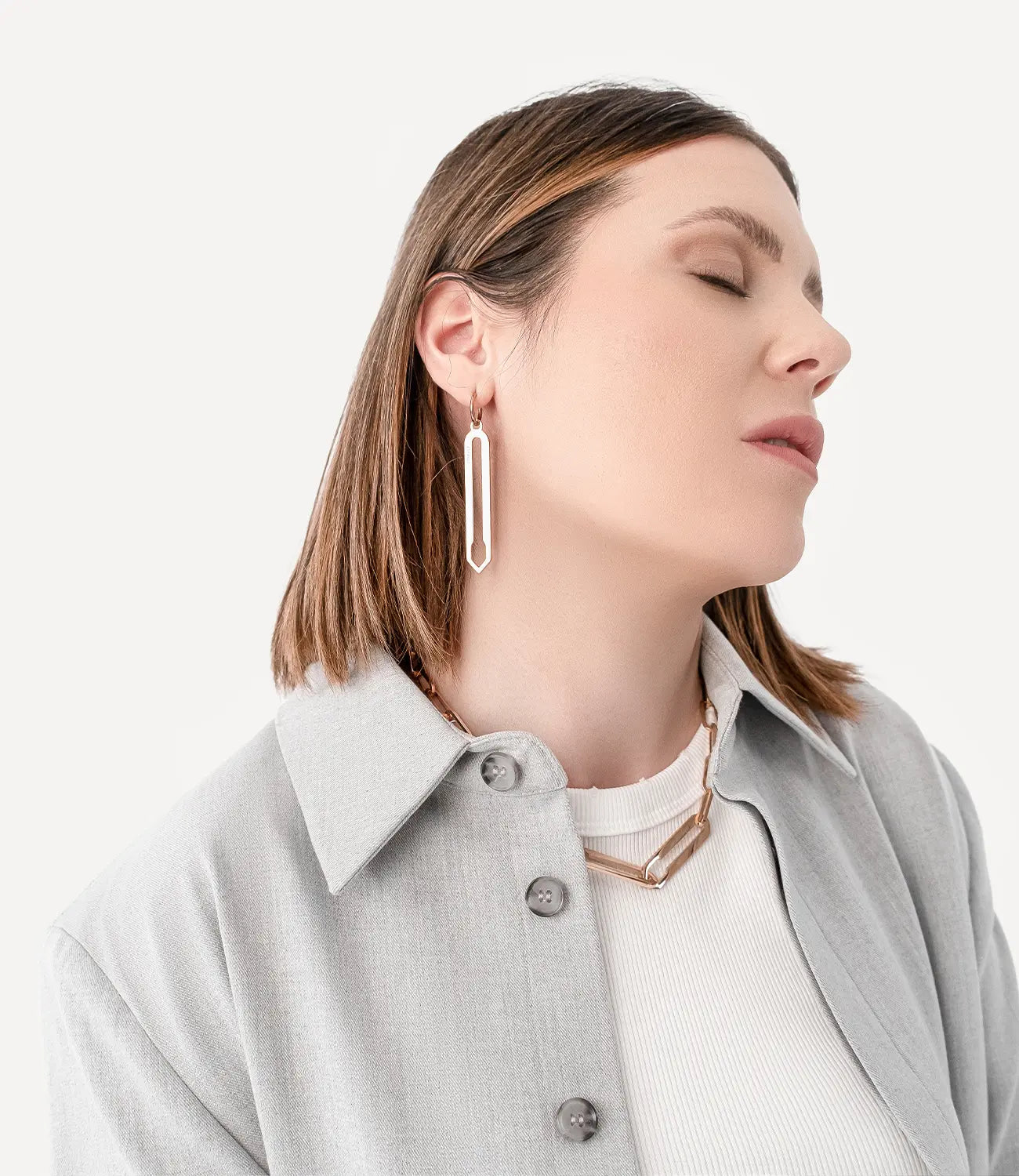Weibliches Model trägt Forma Lamina Ohrringe und Forma Nexus Halskette, beide in Roségold aus hochwertigem 316L-Edelstahl, vor neutralem Hintergrund.