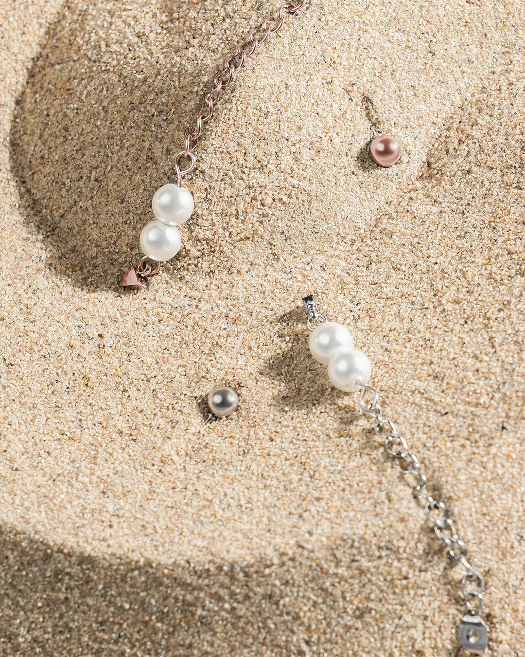 Die Larmes Ohringe in Silber und Roségold liegen auf feinem Sand, vollständige Draufsicht.