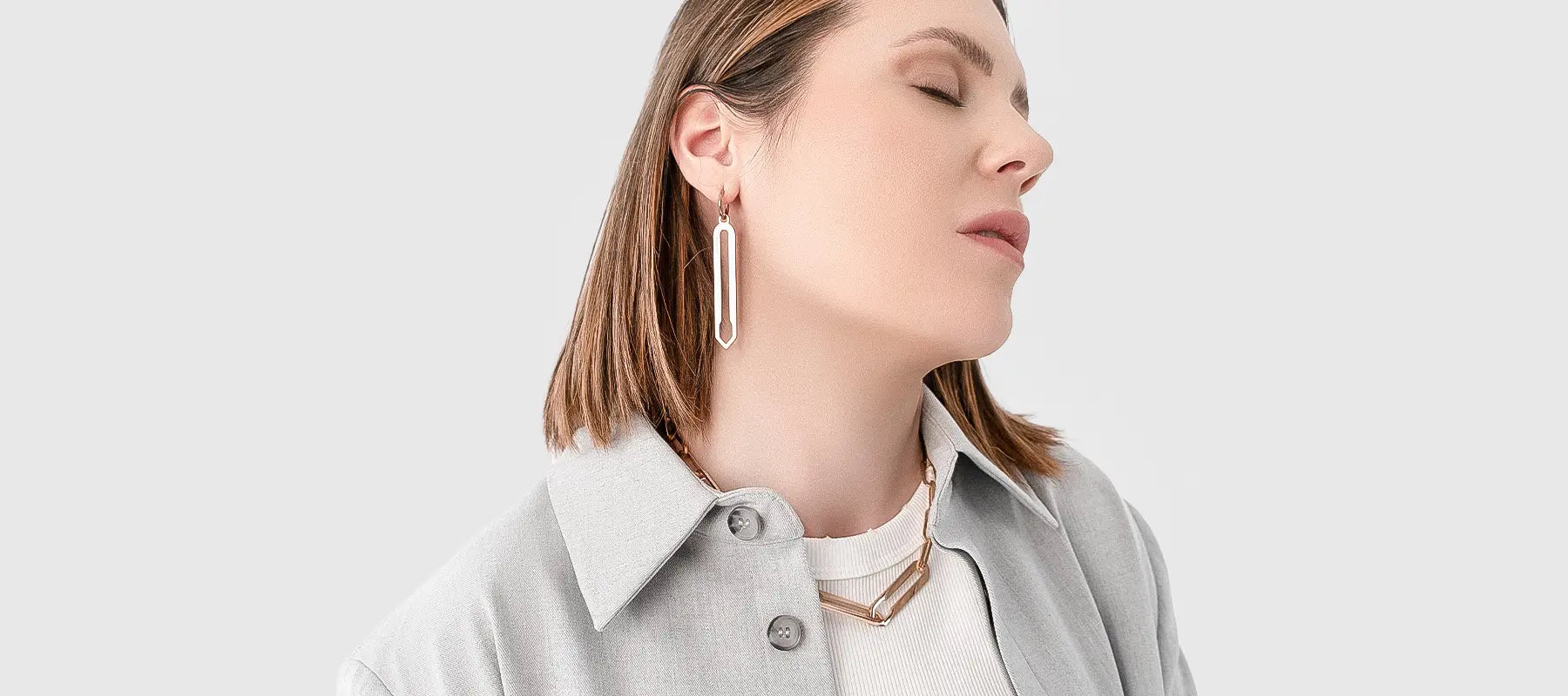 Weibliches Model trägt Forma Lamea Ohrringe und Forma Infini Halskette, beide in Roségold aus hochwertigem 316L-Edelstahl, vor neutralem Hintergrund.